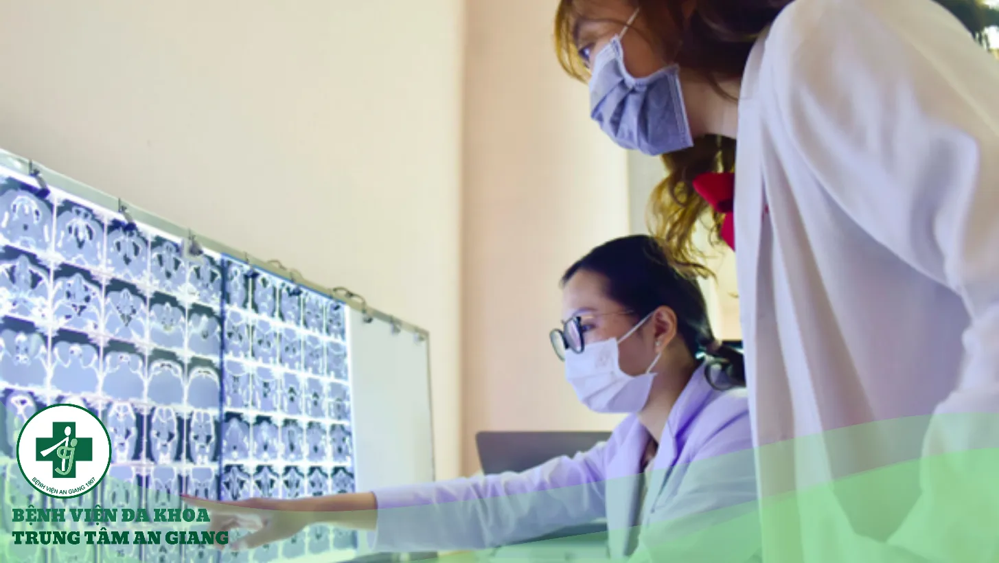 A person wearing a mask and white coat looking at a computer screen Description automatically generated